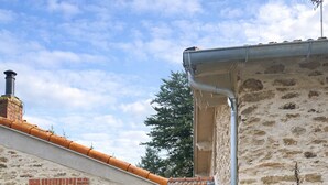 Ein rustikales Steinhaus mit Ziegeldach, einem Holztisch und einer großen Pflanze im Vordergrund.