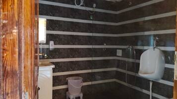Un baño con paredes de mármol a rayas, un lavabo blanco, un pequeño cubo de basura y un orinal.
