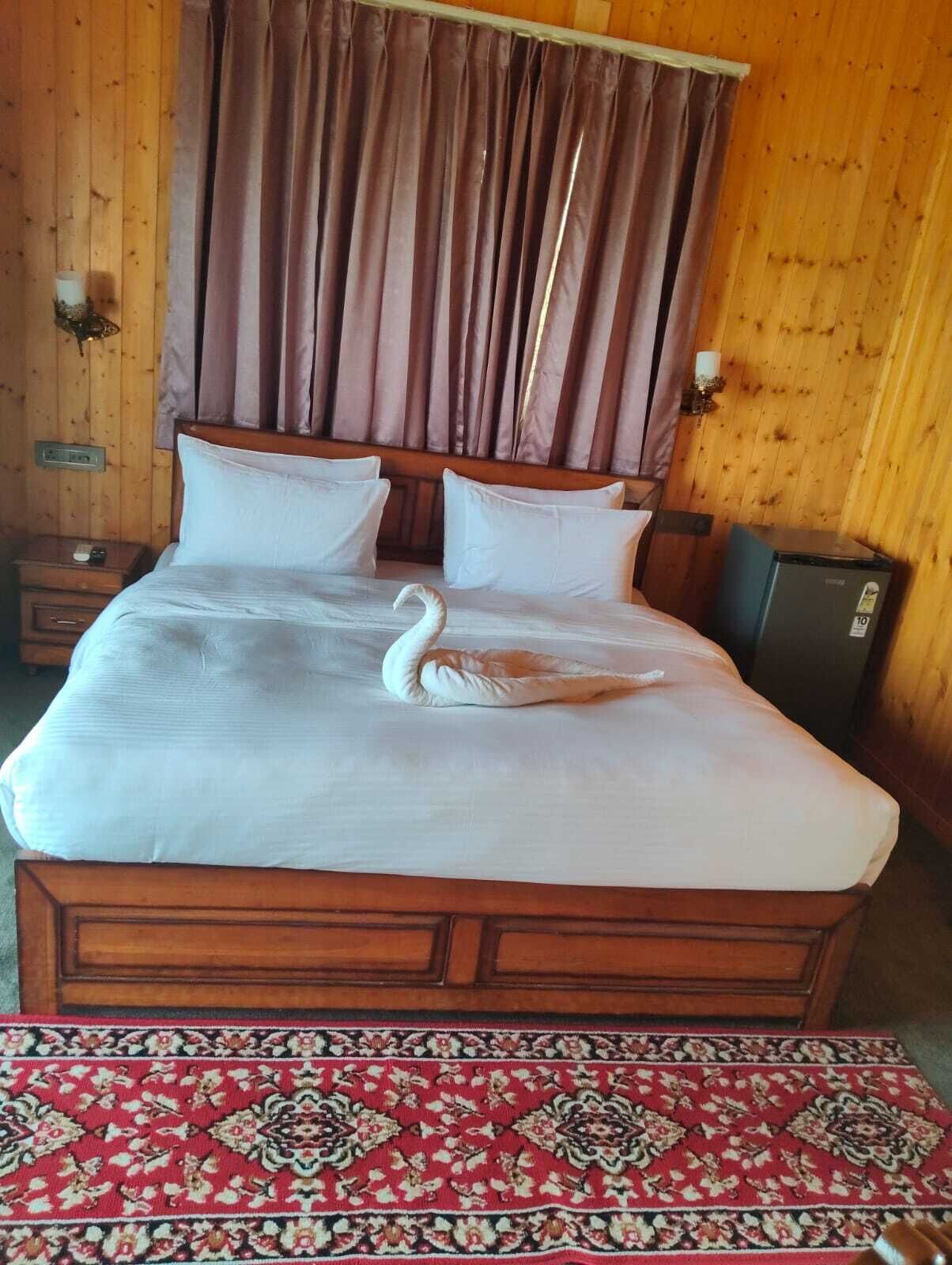 Een kamer met houten lambrisering, een bed, twee nachtkastjes, een tapijt met een rood patroon, en een wandradiator.