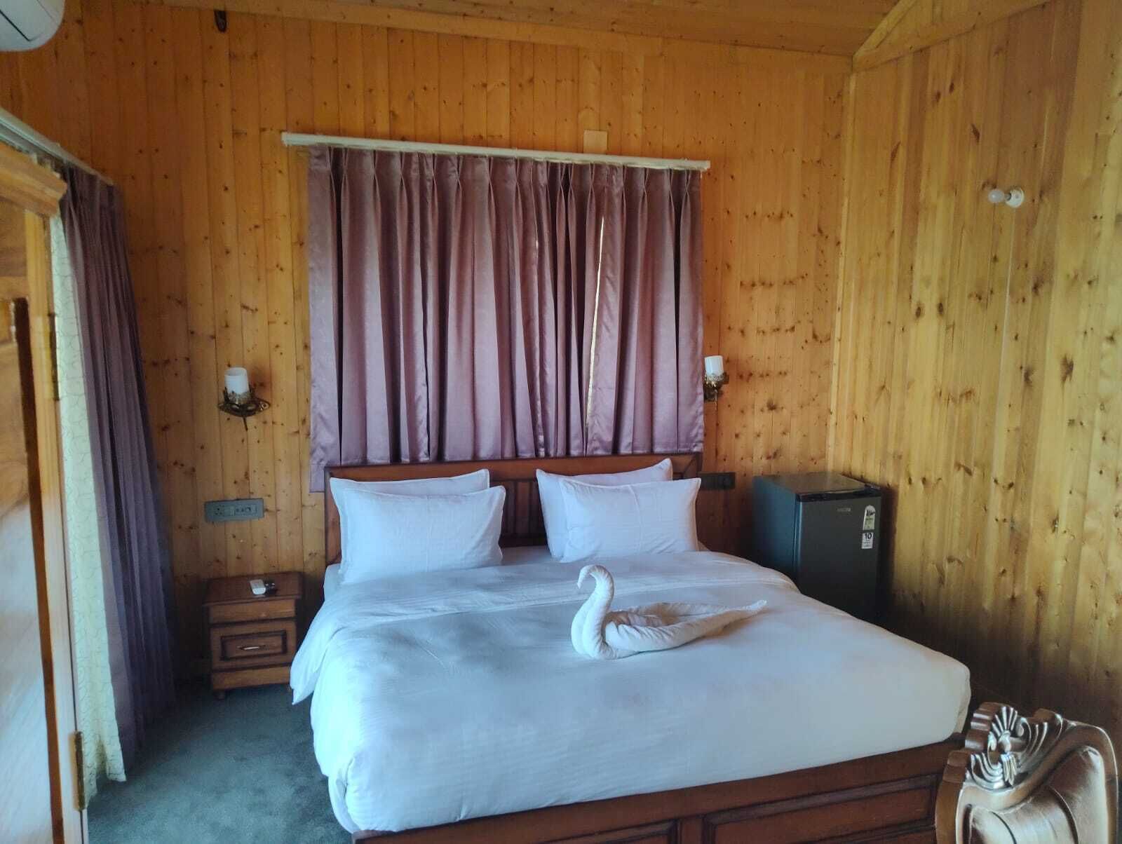 Ein Zimmer mit Holzboden, einem Bett, Vorhängen, einem Nachttisch, einer Kommode und einer dekorativen Schwane auf dem Bett.