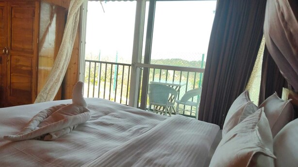 A bed with white linens, a wooden wardrobe, and a balcony with a view of the beach. - Thorn Kitchen &Hideaways (Hoshiarpur)