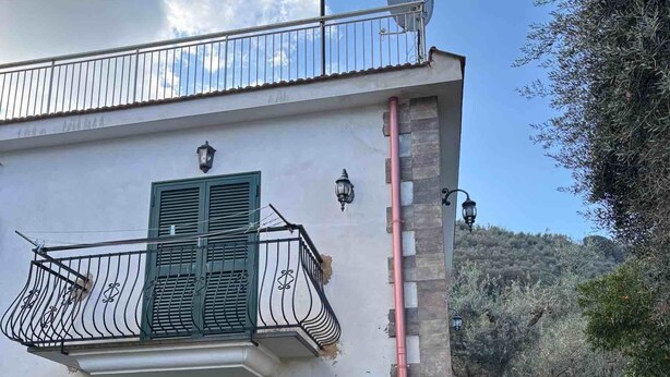 Een gebouw met twee verdiepingen, een balkon, een deur met ruitpanelen en een klein terras.