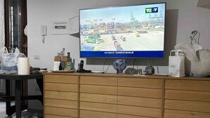 Een kamer met een televisie waarop een nieuwskanaal wordt vertoond, een houten kast en een betegelde vloer.