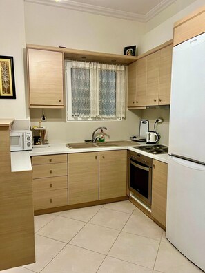 A kitchen with wooden cabinets, a microwave, a kettle, and a refrigerator. - Acropolis Aura Apartment (Athina)