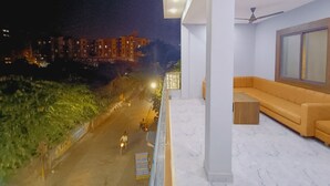 A balcony with a sofa and a table, overlooking a street with buildings and greenery. - Shree Krishna Hotel  (Ujjain)