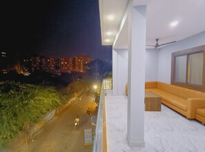 A balcony with a sofa and a table, overlooking a street with buildings and greenery. - Shree Krishna Hotel  (Ujjain)