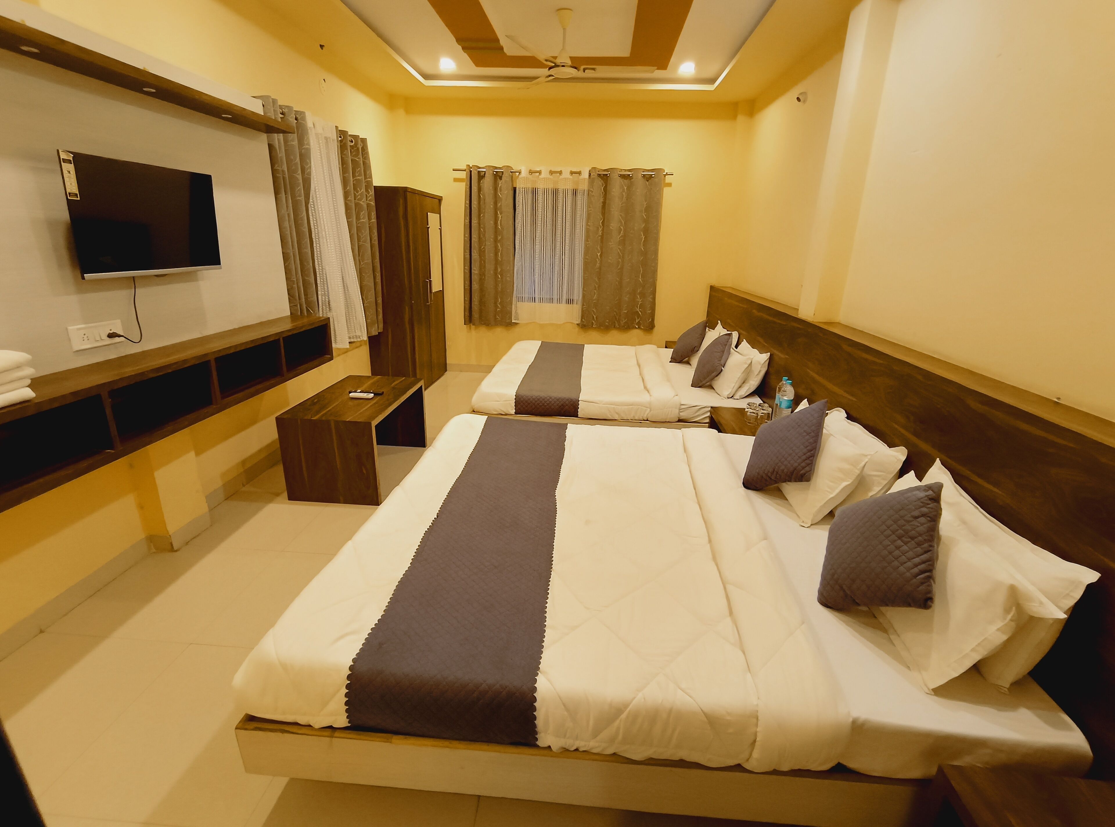 A hotel room with two beds, a TV, a desk, and a window with curtains.