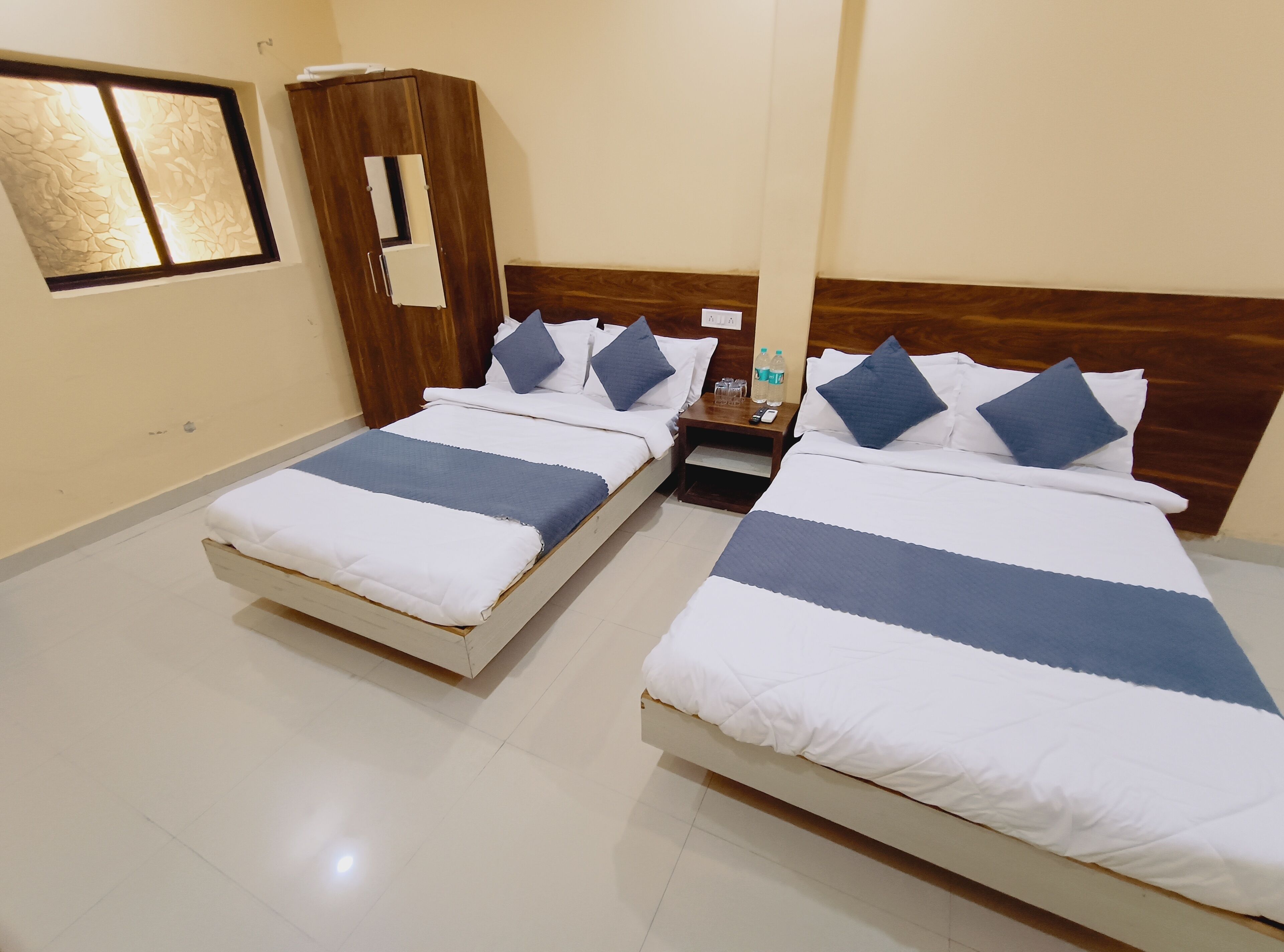 A hotel room with two beds, a wardrobe, a nightstand, and a mirror.