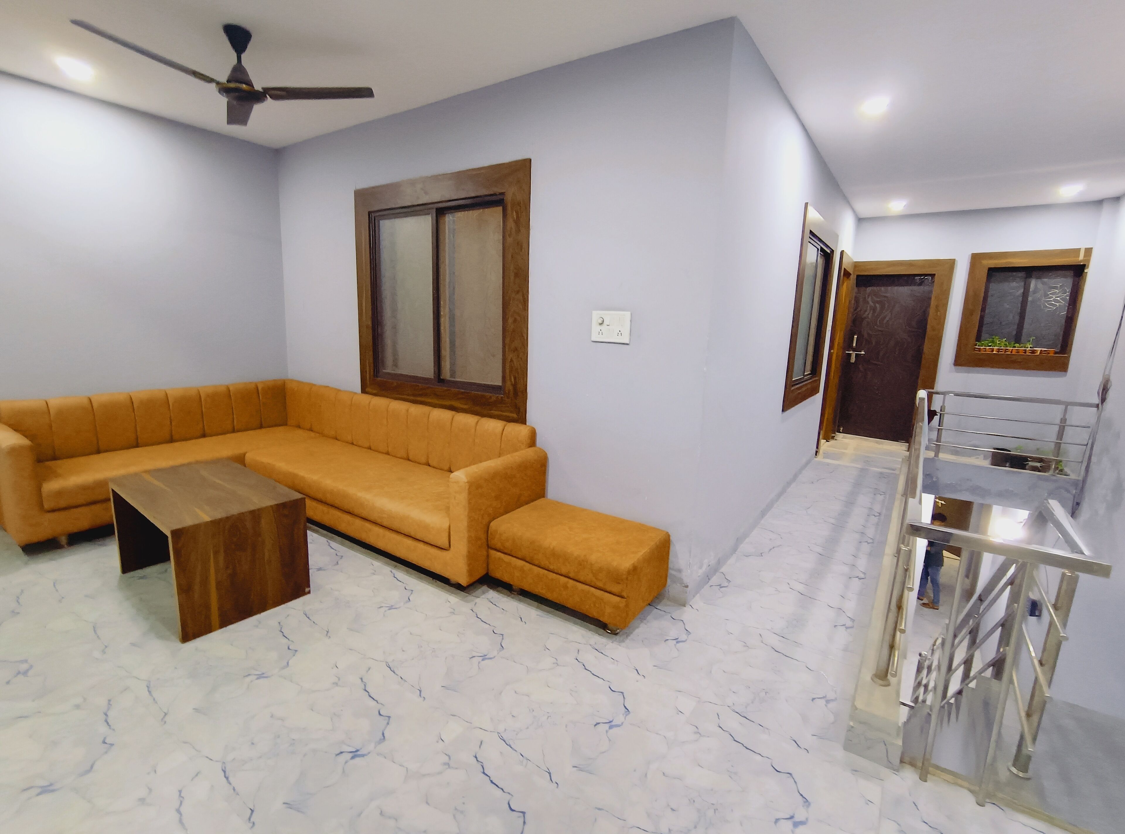 A living room with a sectional sofa, a wooden coffee table, a ceiling fan, and a staircase with a metal railing.