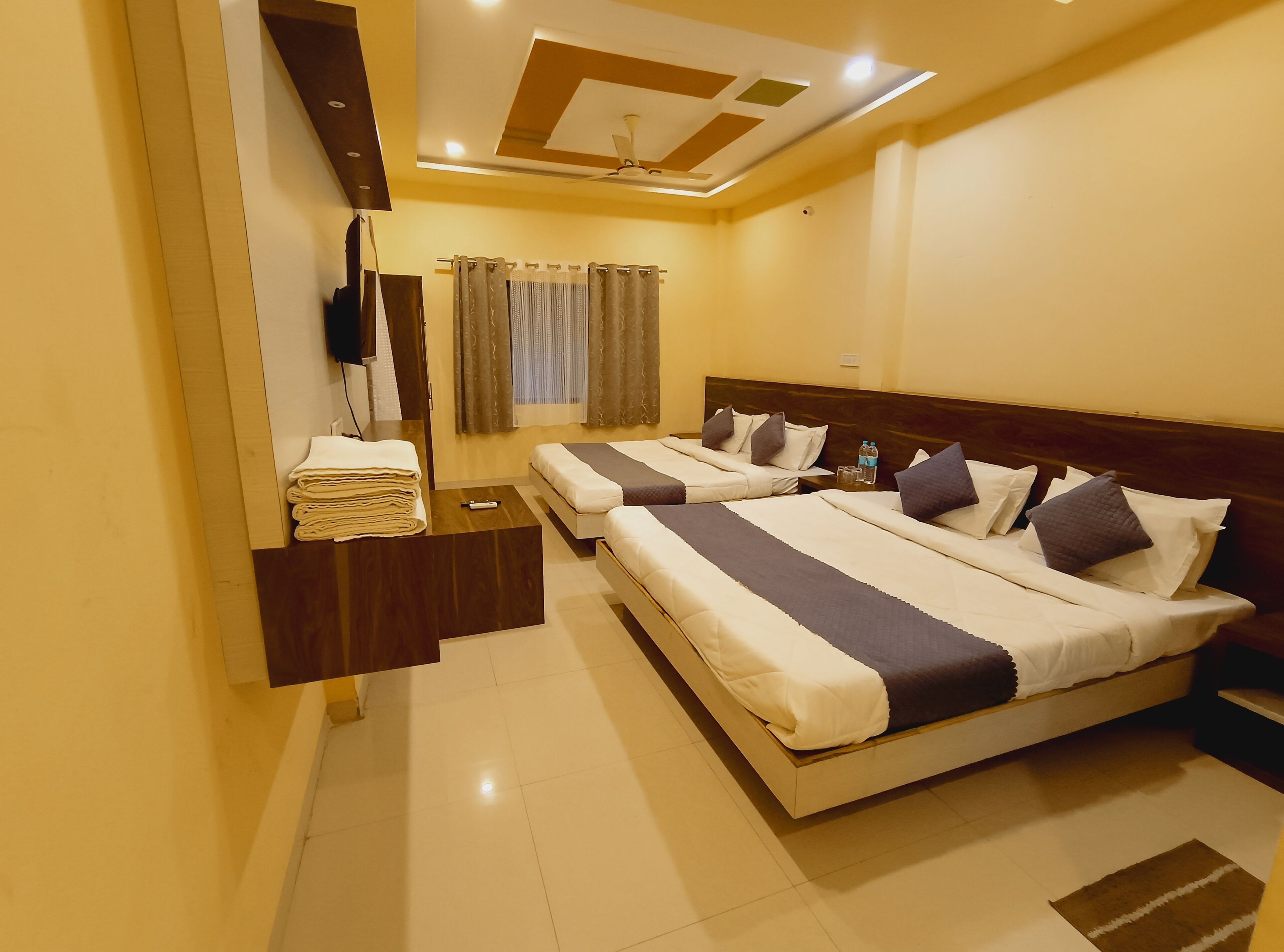 A hotel room with a modern design, featuring a large bed with a wooden headboard, a bedside table with a remote control, and a neatly made bed with towels.