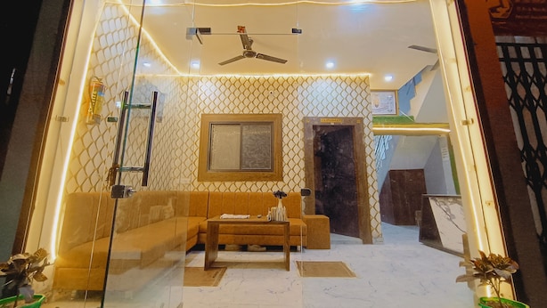 A room with a sofa, a coffee table, a ceiling fan, a window, and a door. - Shree Krishna Hotel  (Ujjain)