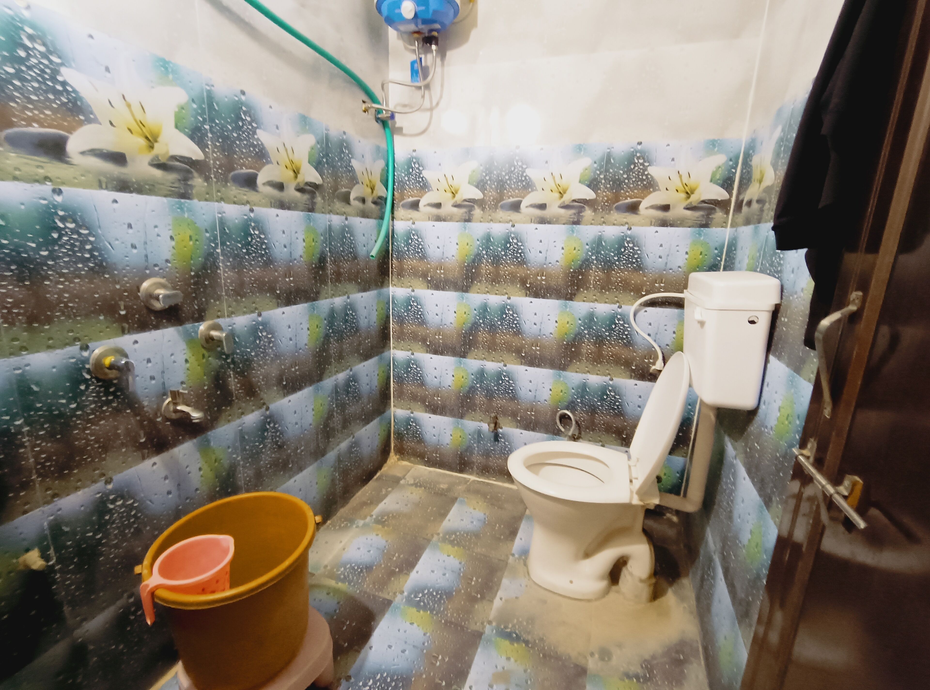 Une petite salle de bain avec des toilettes, un seau et un tuyau de douche.