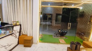A room with a glass door leading outside, a small seating area with a sofa and a table, and a decorative plant on the windowsill. - Shree Krishna Hotel  (Ujjain)