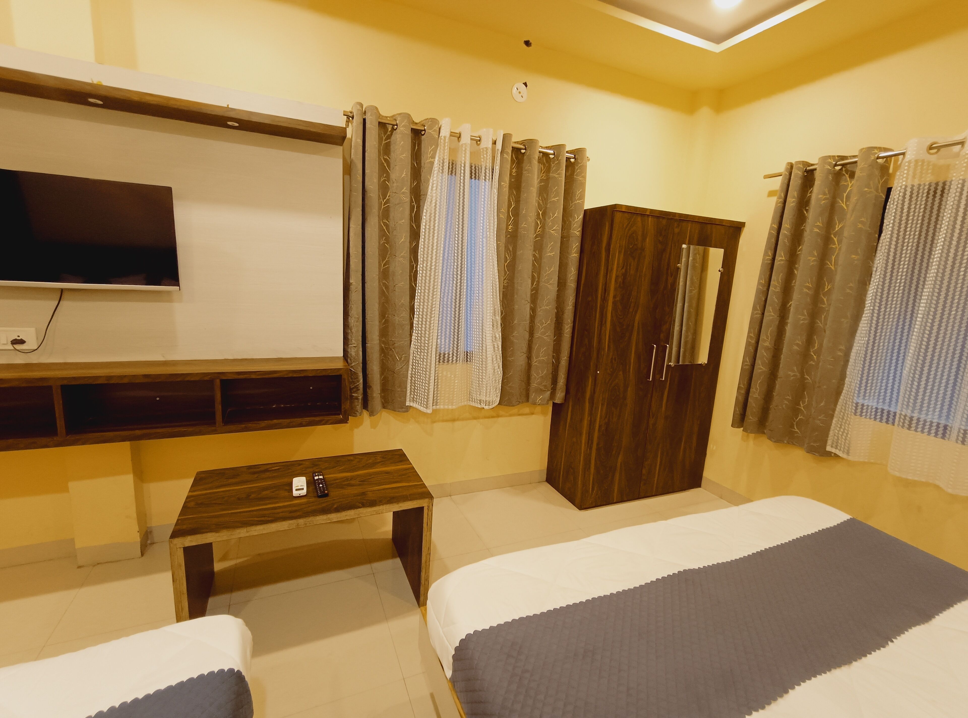 A hotel room with a bed, a TV, a wooden desk, a wardrobe, and curtains.