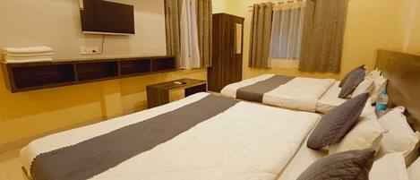 Quarto de hotel com duas camas, televisão de tela plana, mesa de cabeceira de madeira, guarda-roupa e ventilador de teto.