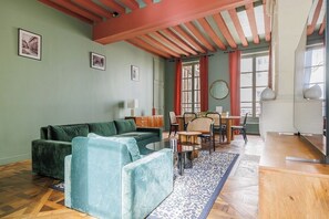 Ein Wohnzimmer mit einem grünen Sofa, einem blauen Sessel, einem Holztisch und einem Essbereich mit Tisch und Stühlen.