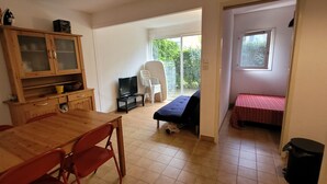 A room with a wooden dining table, red chairs, a TV, a sofa, and a bed. - T2 cabin apartment on garden level with pedestrian access to the beach (Agde)