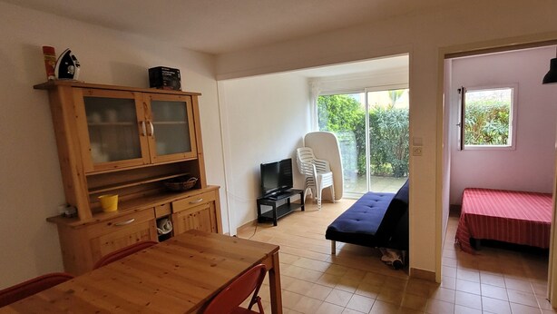 A room with a wooden dining table, a television, a sofa, and a bed. - T2 cabin apartment on garden level with pedestrian access to the beach (Agde)