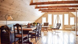 A wooden interior with a dining table, chairs, a lamp, and a window with a view.