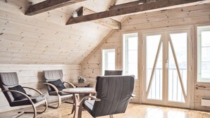 A loft-style room with wooden beams, a high ceiling, and large windows.