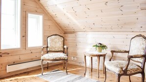 A room with wooden walls and a sloped ceiling, featuring two ornate chairs and a small table with a vase of flowers.