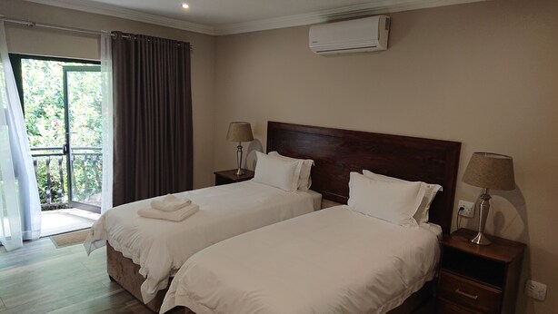 Een hotelkamer met twee bedden, een balkon met gordijnen, een airconditioning en bedlampen.