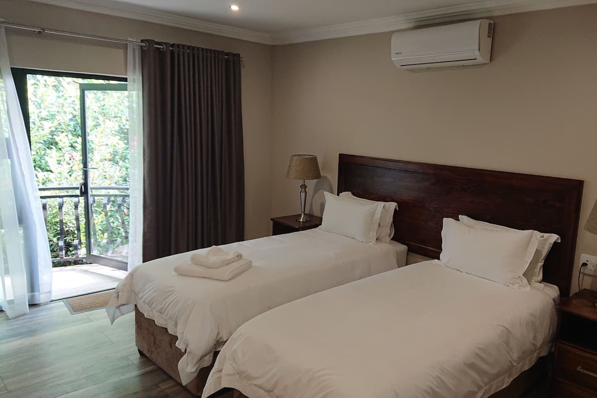 Una habitación de hotel con dos camas, un balcón con cortinas, un equipo de aire acondicionado y lámparas de noche.