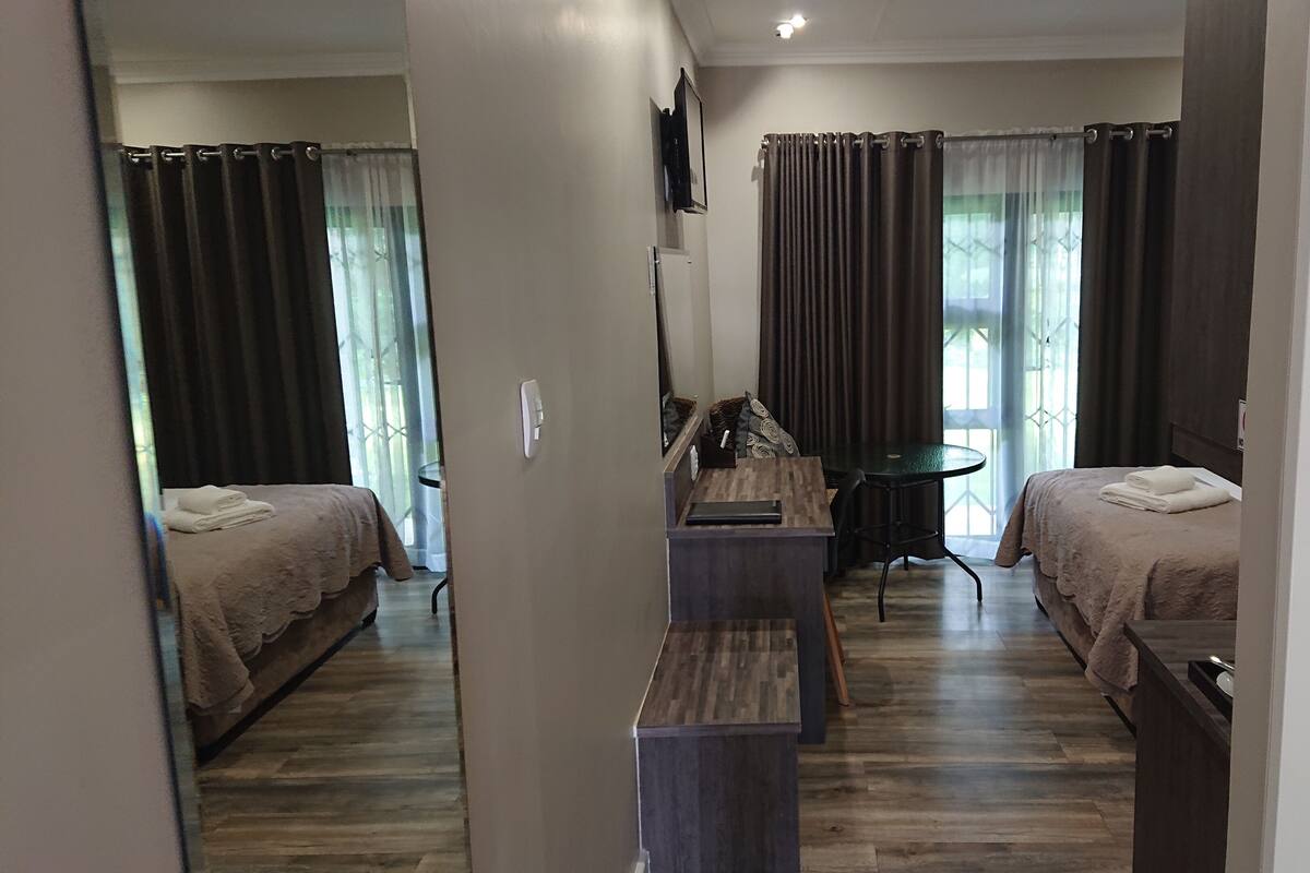 Habitación de hotel con dos camas, un escritorio, una silla, una mesita y un televisor.
