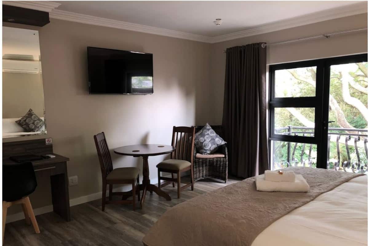 Habitación de hotel con cama, escritorio, silla, televisión y balcón con cortinas.