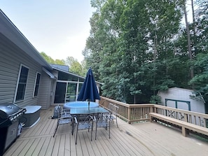 A deck with a grill, table, and umbrella, surrounded by trees.