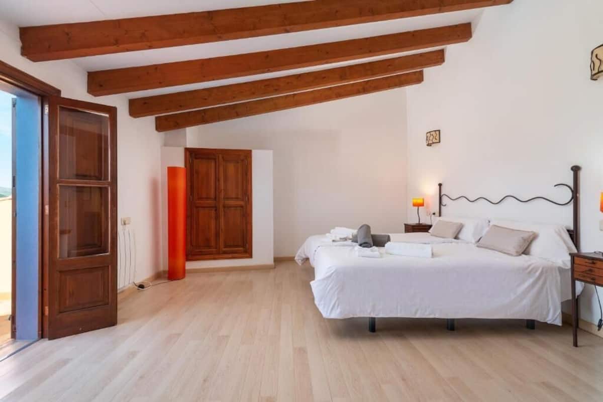 Un dormitorio con techo de madera, una cama con ropa de cama blanca, una mesita de noche y una lámpara.