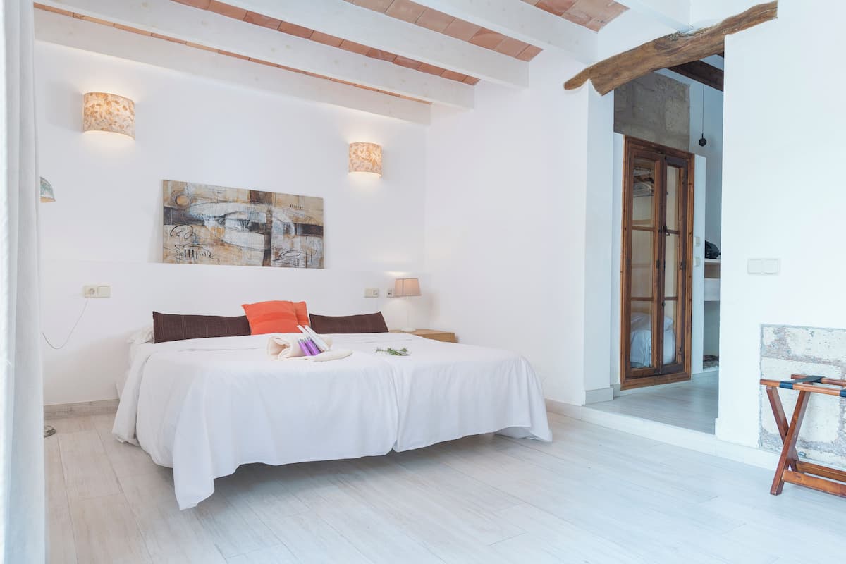 Un dormitorio con una cama, dos lámparas de pared, un cuadro y una viga de techo de madera.