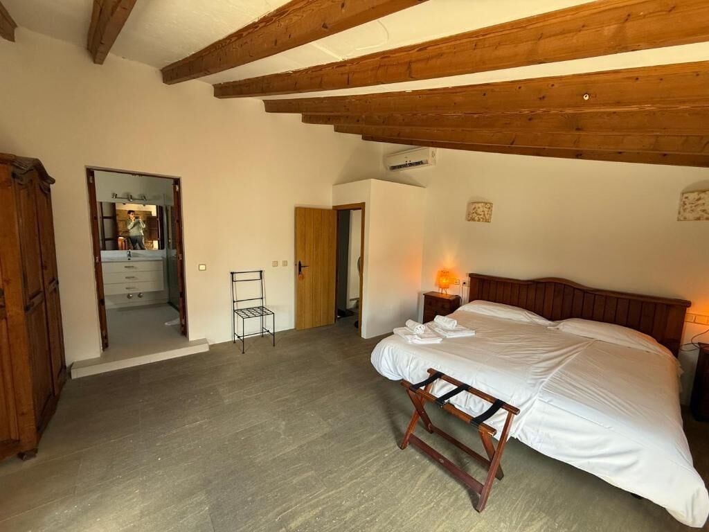 A bedroom with a bed, wooden beams, a nightstand, a lamp, and a mirror.