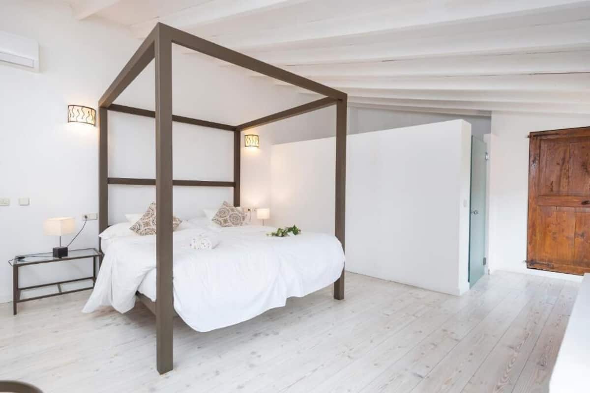 Un dormitorio con cama con dosel, lámparas de noche, una mesita de noche y un armario de madera.