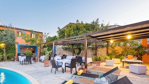 Un área de comedor al aire libre con mesas y sillas, una piscina y una pérgola con luces.