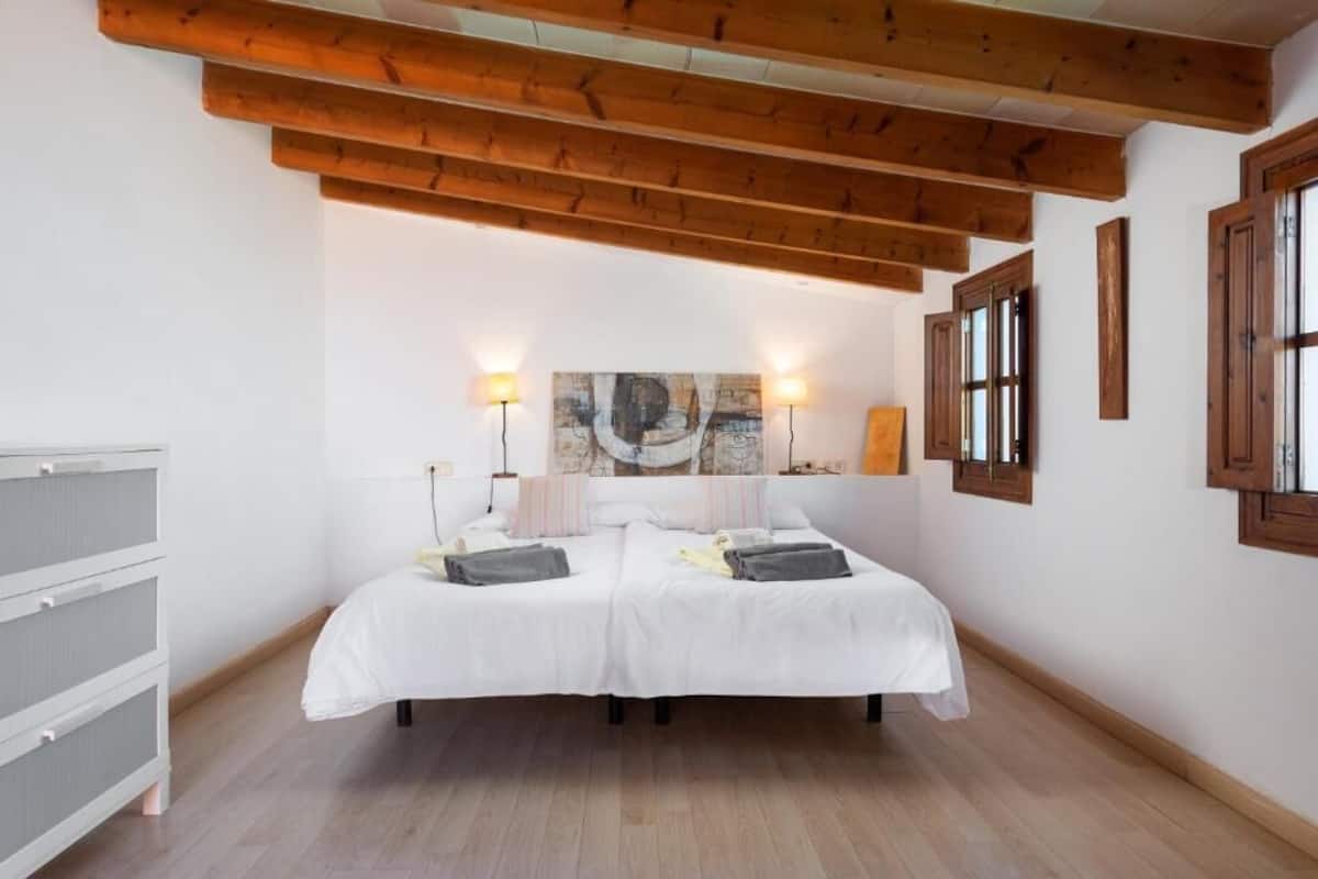 Un dormitorio con techo de madera, dos camas, lámparas de noche y un cuadro abstracto grande en la pared.