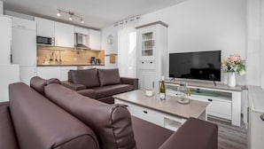 A modern living room with a sofa, a TV, a dining table, and a kitchen area with cabinets and appliances. - Bahnhofstraße 10 - Apartment 3 - Holiday apartment in Zingst with balcony near the beach (Zingst)