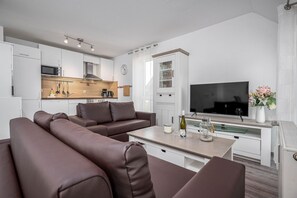 Ein modernes Wohnzimmer mit einer Couch, einem Fernseher, einem Esstisch und einer Küchenzeile mit Schränken und Geräten.