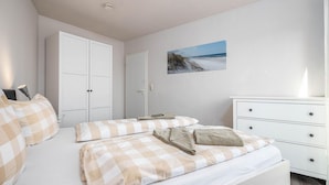 A bedroom with a bed, a dresser, a wardrobe, and a painting of a beach scene. - Bahnhofstraße 10 - Apartment 3 - Holiday apartment in Zingst with balcony near the beach (Zingst)