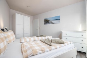 Ein Schlafzimmer mit einem Bett, einem Schminktisch, einem Kleiderschrank und einem Bild von einer Strandansicht.