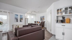 A modern living room with a brown sofa, dining area, kitchen with cabinets, and artwork on the walls. - Bahnhofstraße 10 - Apartment 3 - Holiday apartment in Zingst with balcony near the beach (Zingst)