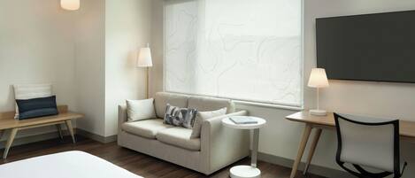 A modern hotel room with a sofa, a small round table, a desk, and a chair.