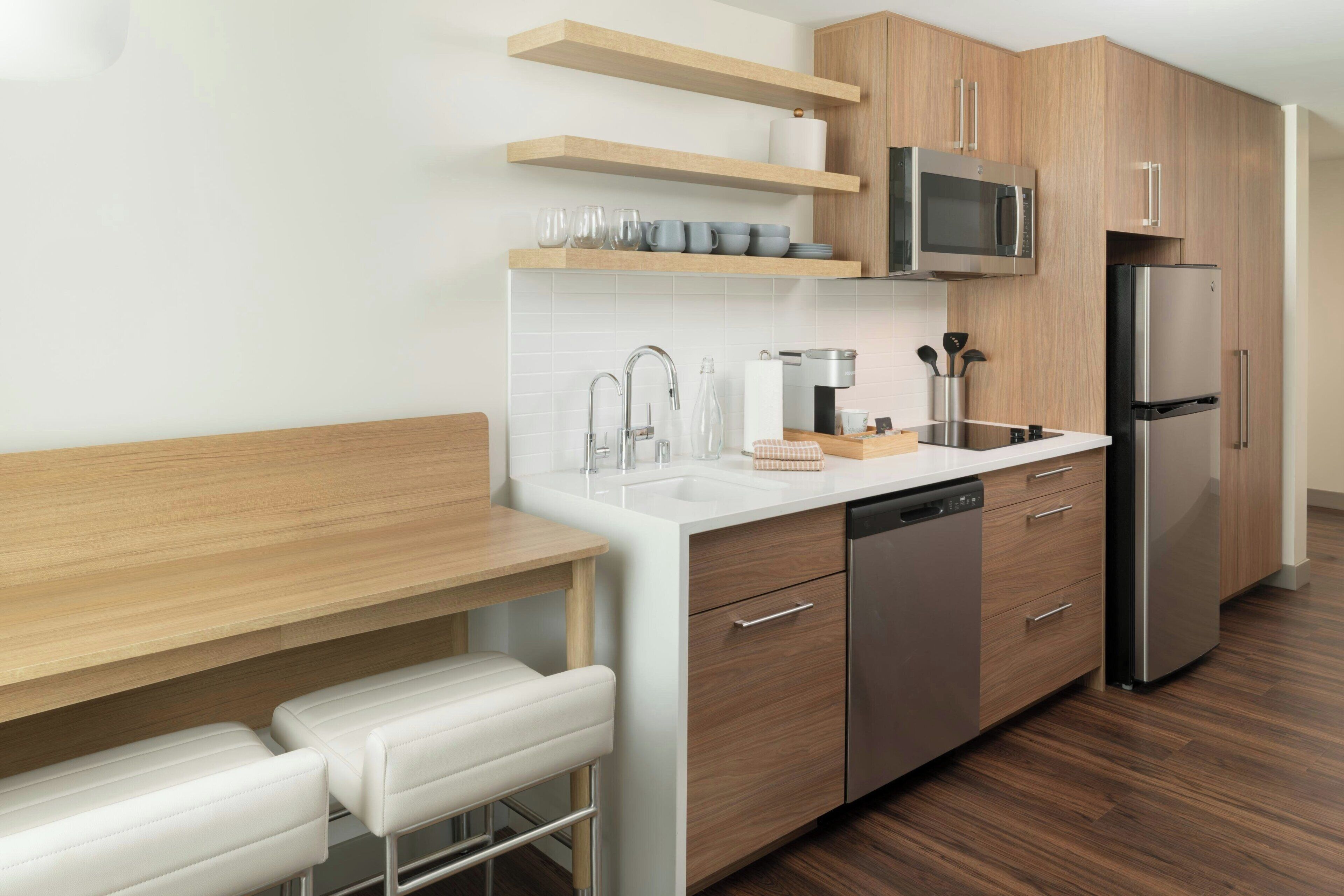 A modern kitchen with wooden cabinets, stainless steel appliances, a white countertop, and a built-in bench with white cushions.