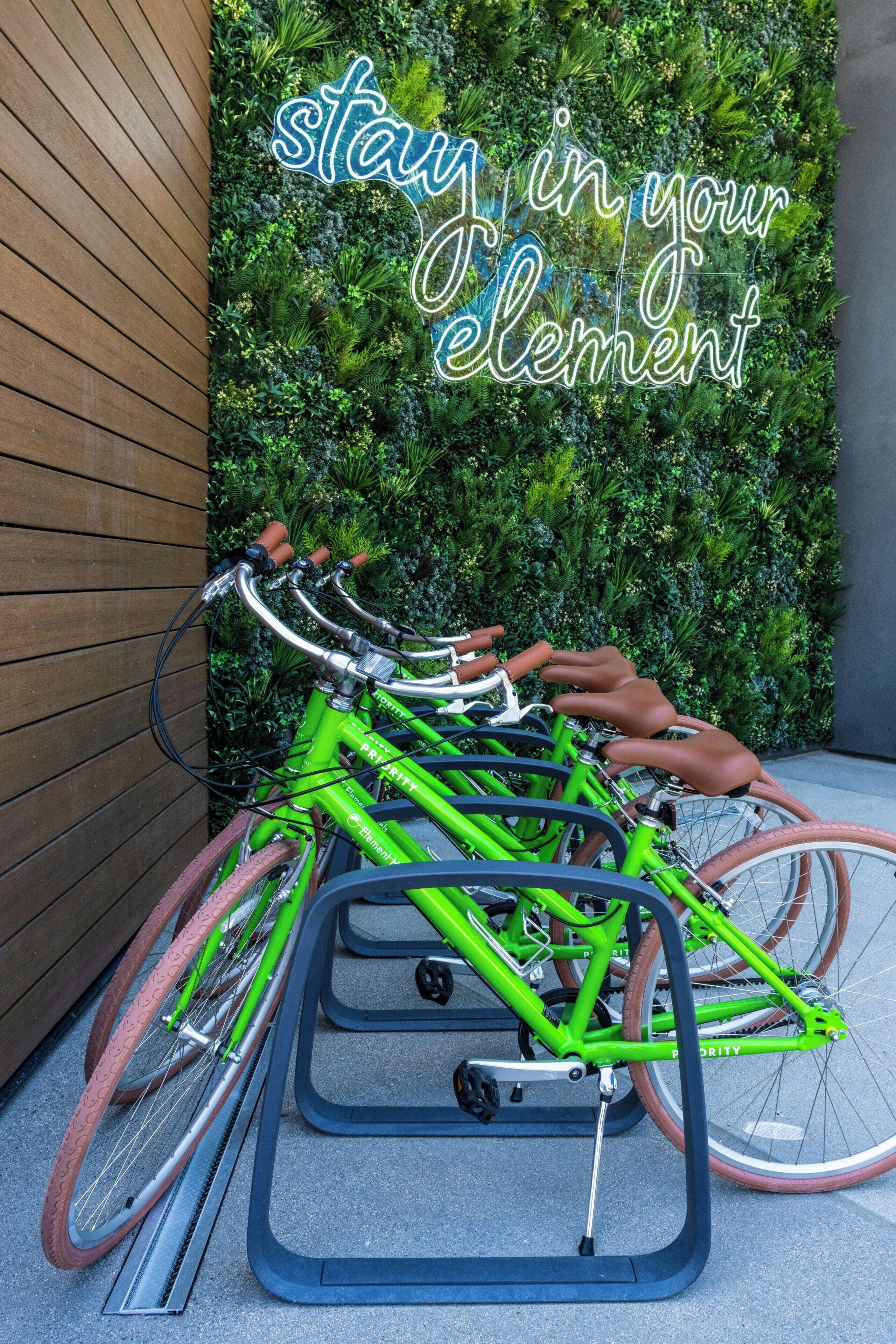 A green bicycle parked in a rack with a sign that reads 'stay in your element' in the background.