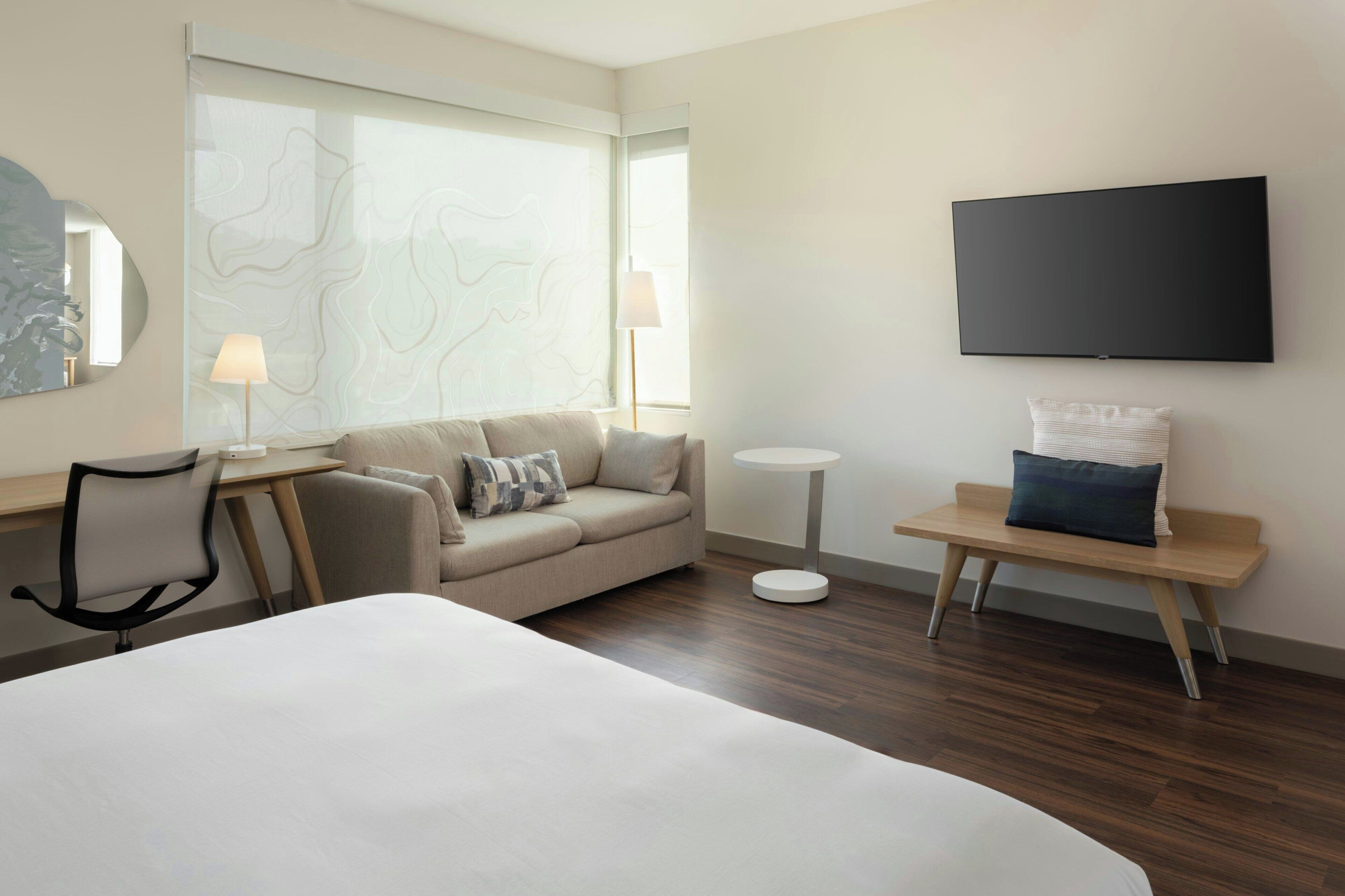 A hotel room with a bed, a sofa, a desk, a chair, a TV, and a small table.