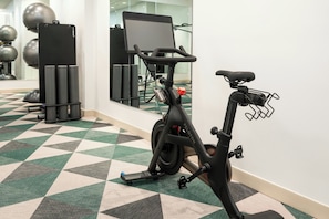 Una bicicleta estática en un gimnasio con un espejo en la pared y pelotas de ejercicio al fondo.