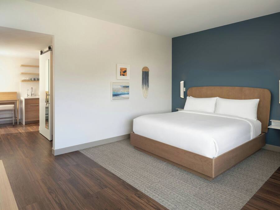 A modern bedroom with a large bed, a wooden headboard, a small desk, and a chair.