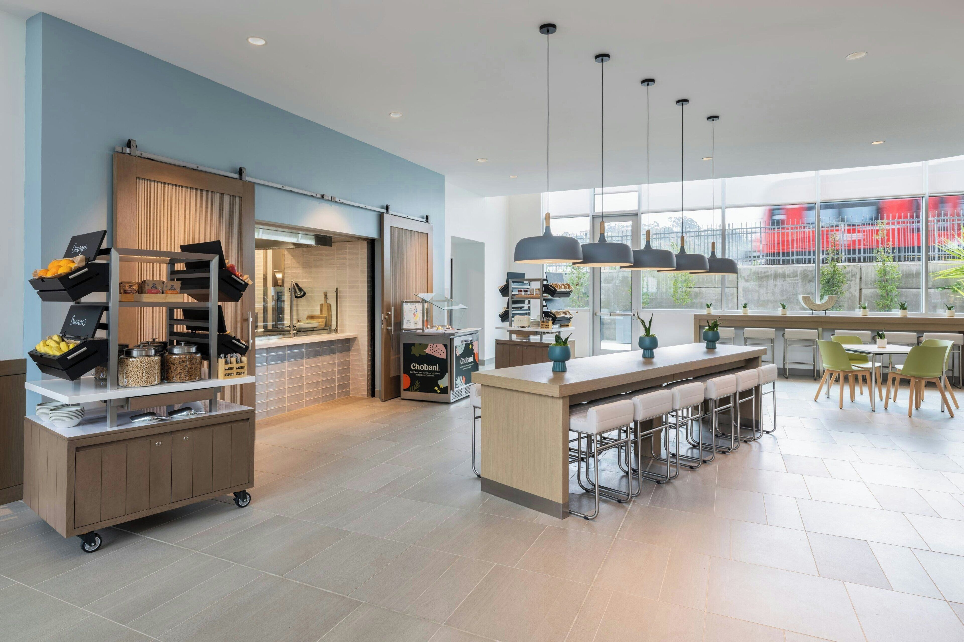 A modern kitchen with a bar area, large windows, and a view of a red train outside.