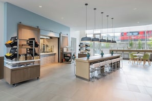 A modern kitchen with a bar area, large windows, and a view of a red train outside. - Element by Marriott San Diego Mission Valley (San Diego)