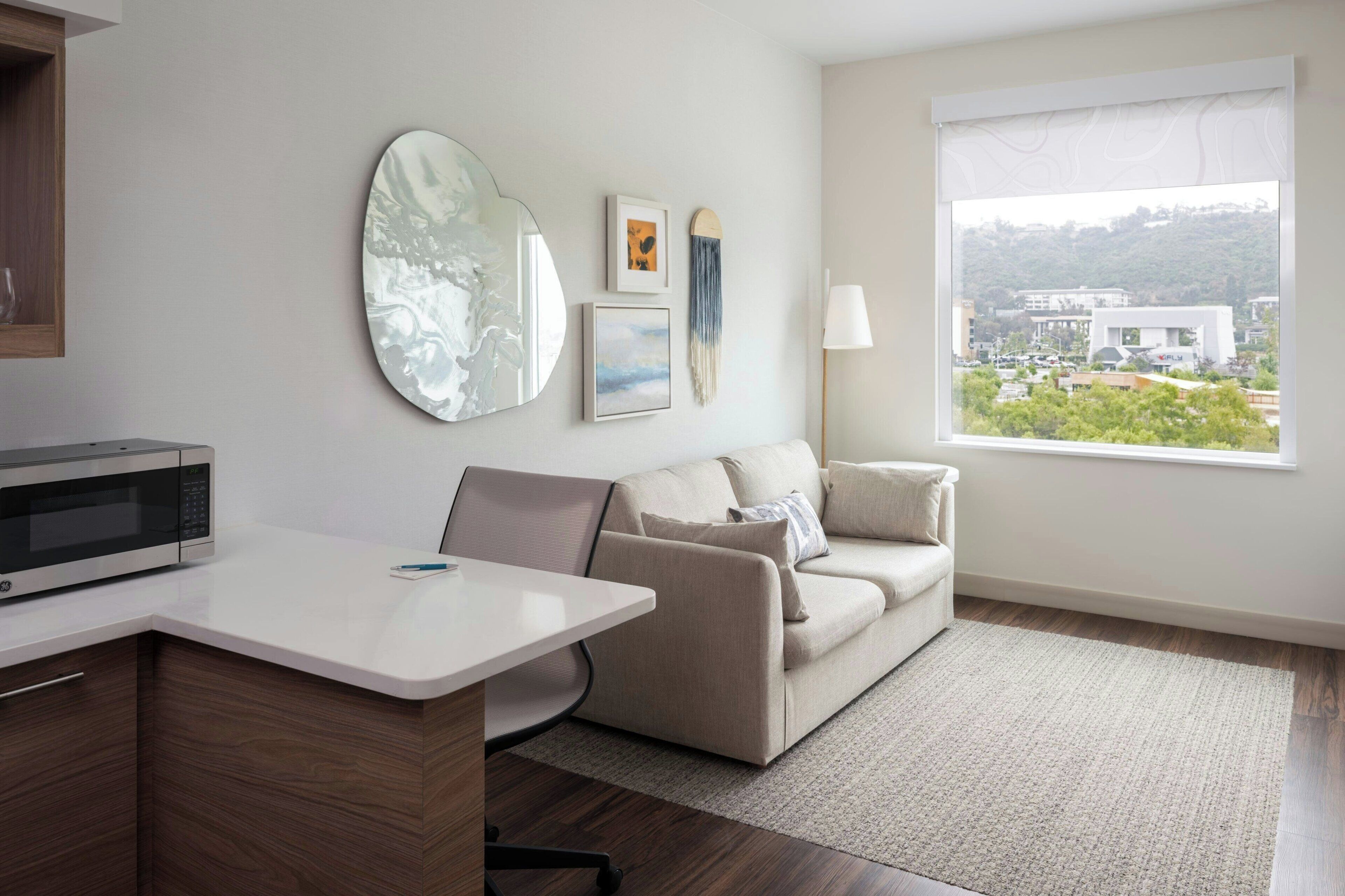Una sala de estar moderna con un sofá, una mesa de centro, un microondas y un ventanal con vistas a edificios.
